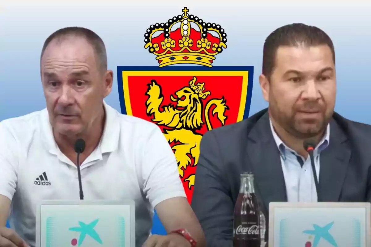 Dos hombres en una conferencia de prensa con el escudo de un león coronado detrás de ellos.